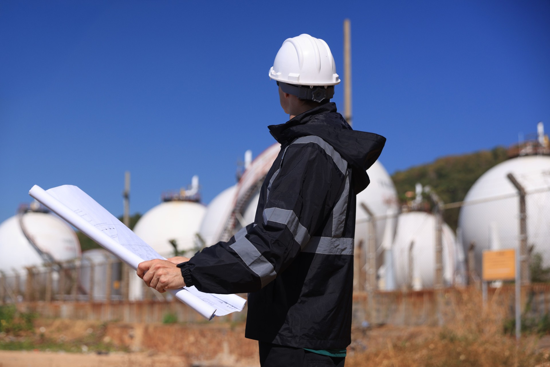 Project engineer in a refinery oil and gas LNG tank, Engineer works with a blueprint and uses walkie talkie at the oil storage tanks site.